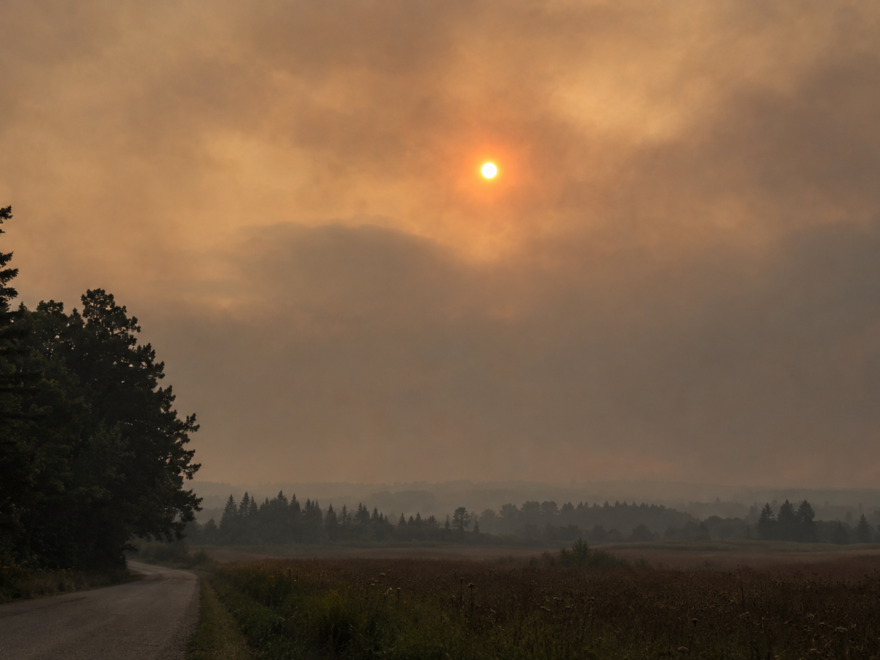 A winding rural road through fields under a smoky sunset